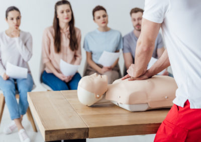 Healthcare training center instructor demonstrating CPR chest compressions on a manikin while students observe during a ACLS certification class.